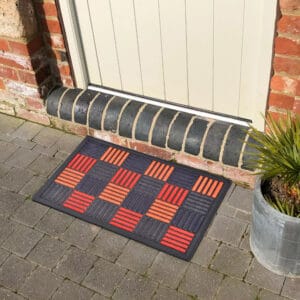 Checkered front door mat placed outside an entryway on stone paving