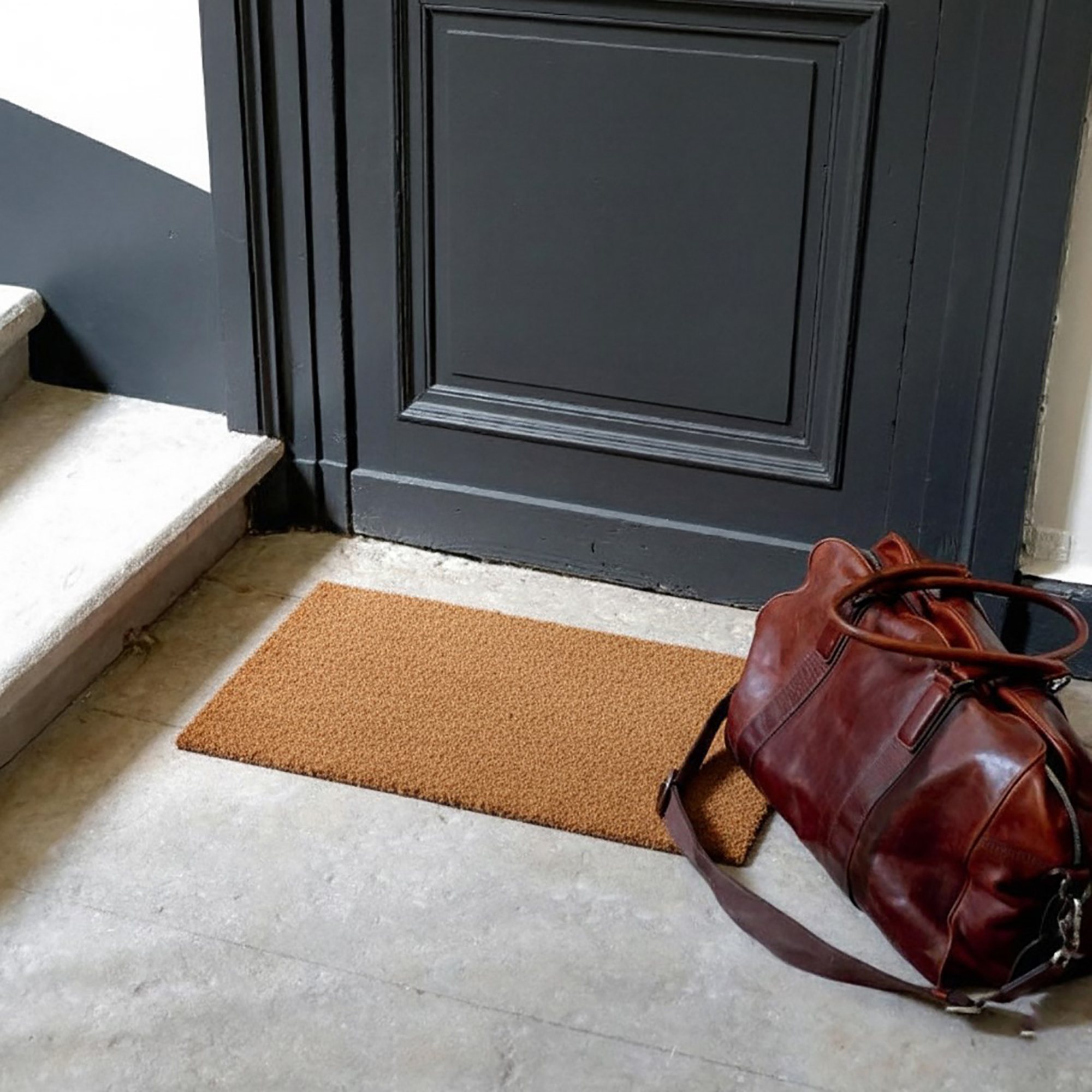 “Compact coir doormat at indoor entry beside leather bag”