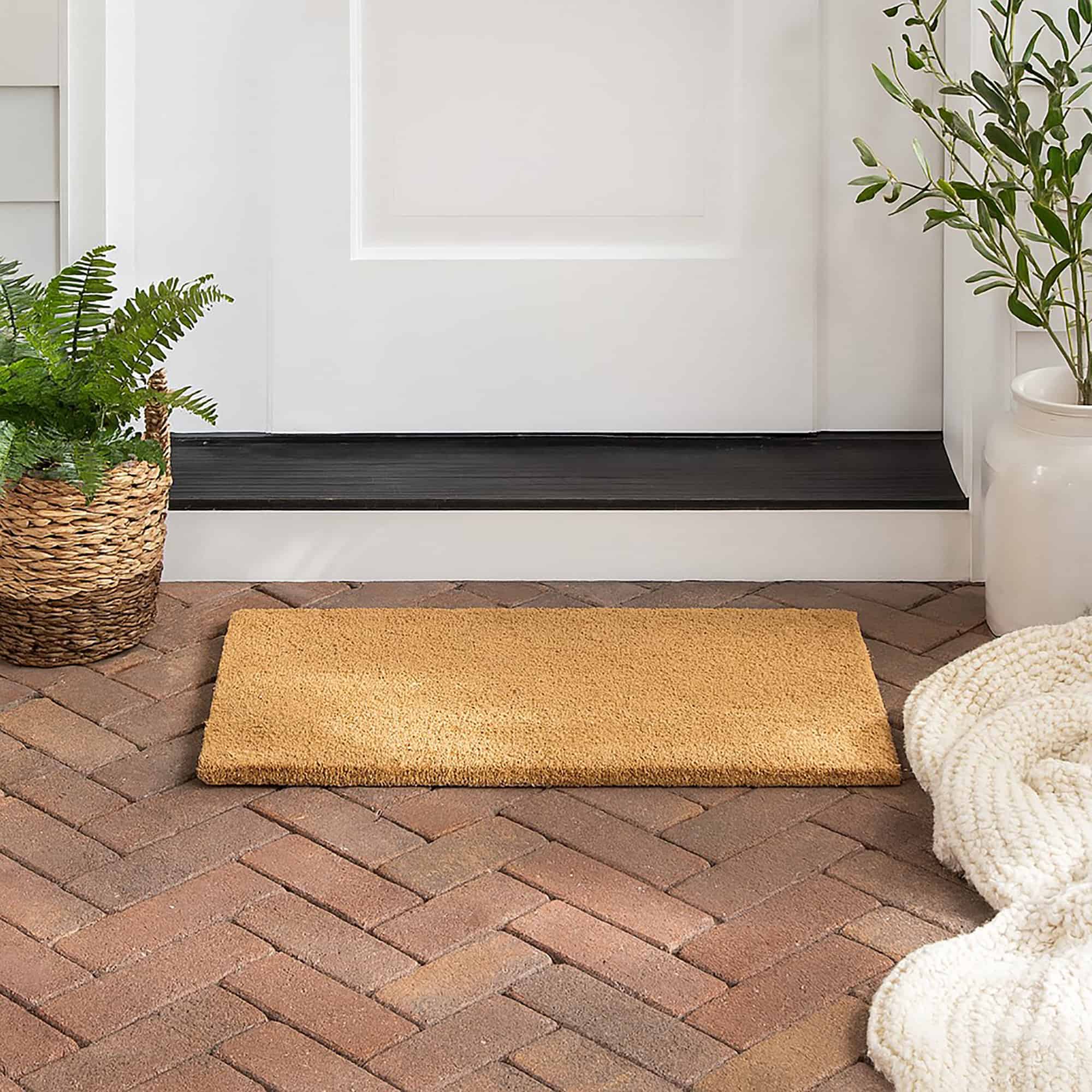 “Coir doormat styled on brick porch near plants”
