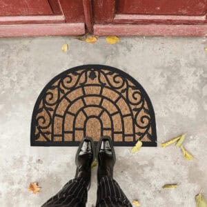 Feet standing on half-round rubber and coir doormat by a red door