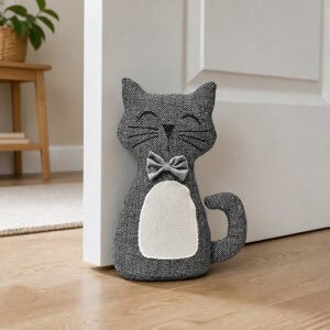 Charcoal cat door stopper propping open a white paneled door in a hallway, hardwood floor, wooden side table with potted plant in the background.