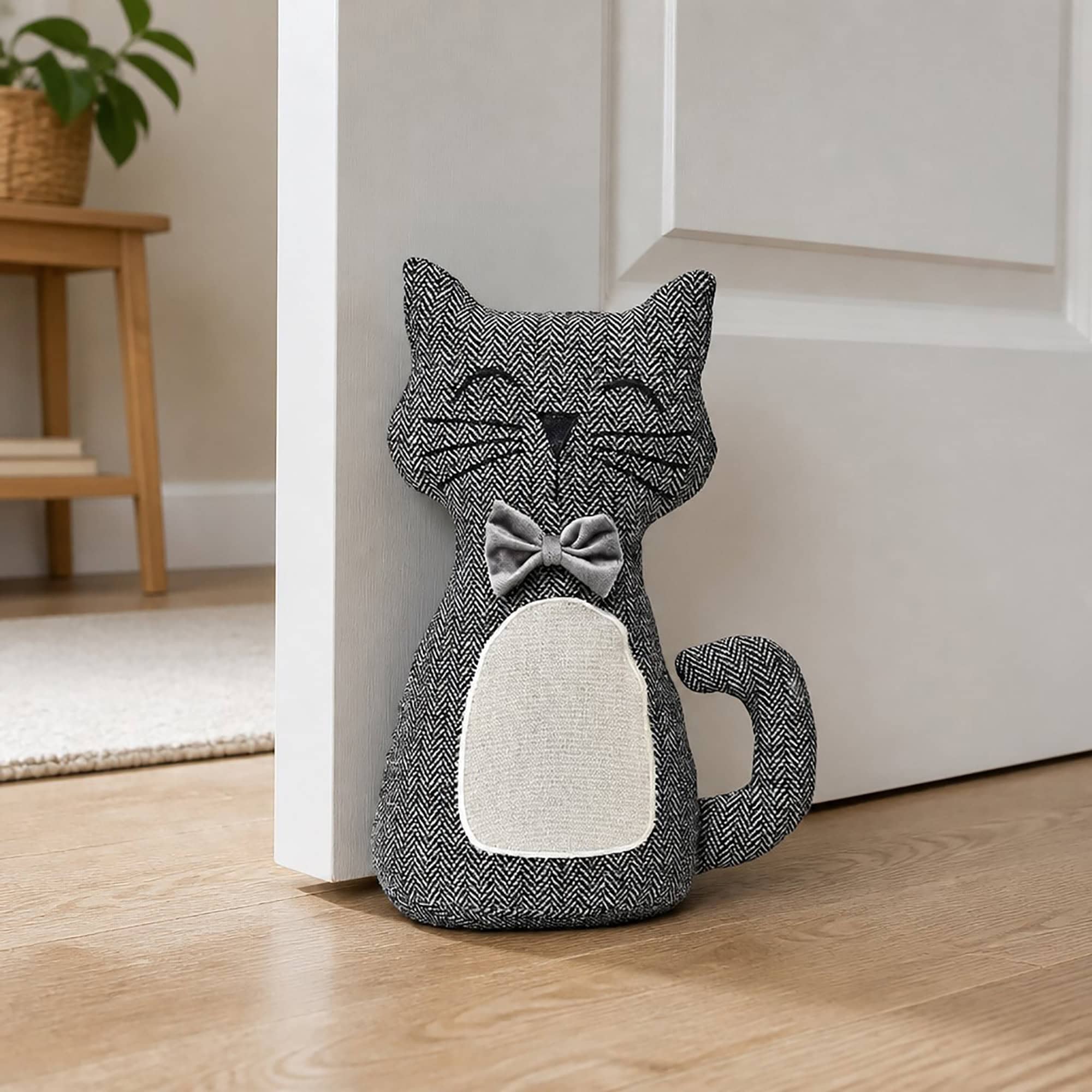 Charcoal cat door stopper propping open a white paneled door in a hallway, hardwood floor, wooden side table with potted plant in the background.