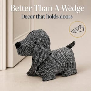 Charcoal dog door stopper propping open a cream paneled door, with a wedge icon. On-image text: "Better Than A Wedge," "Decor that holds doors."