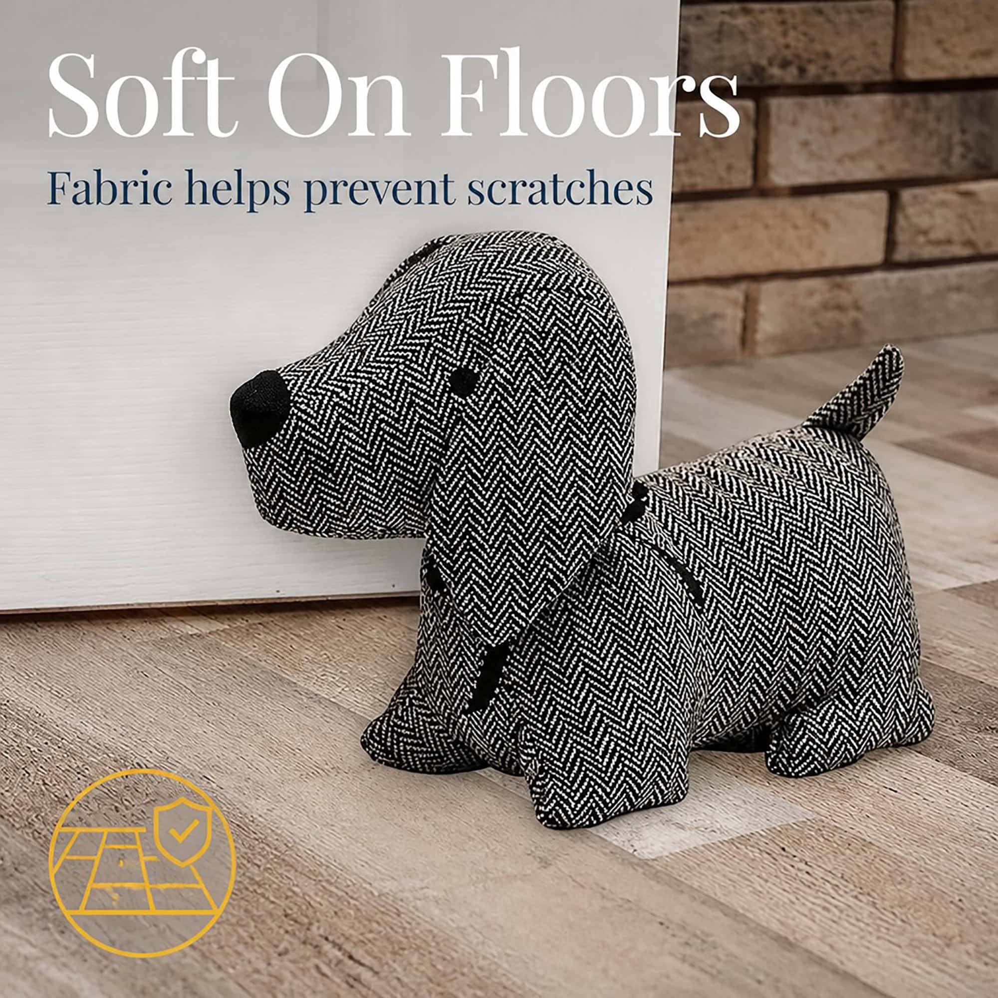 Charcoal dog door stopper against a white door on hardwood floor, brick wall behind, with a floor-protection icon. On-image text: "Soft On Floors," "Fabric helps prevent scratches."