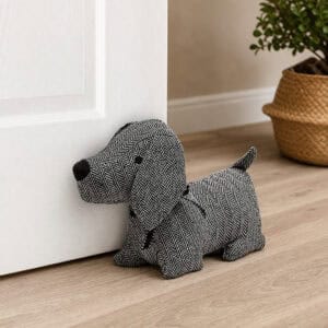 Charcoal dog door stopper propping open a white paneled door, hardwood floor, woven basket with a plant in the background.