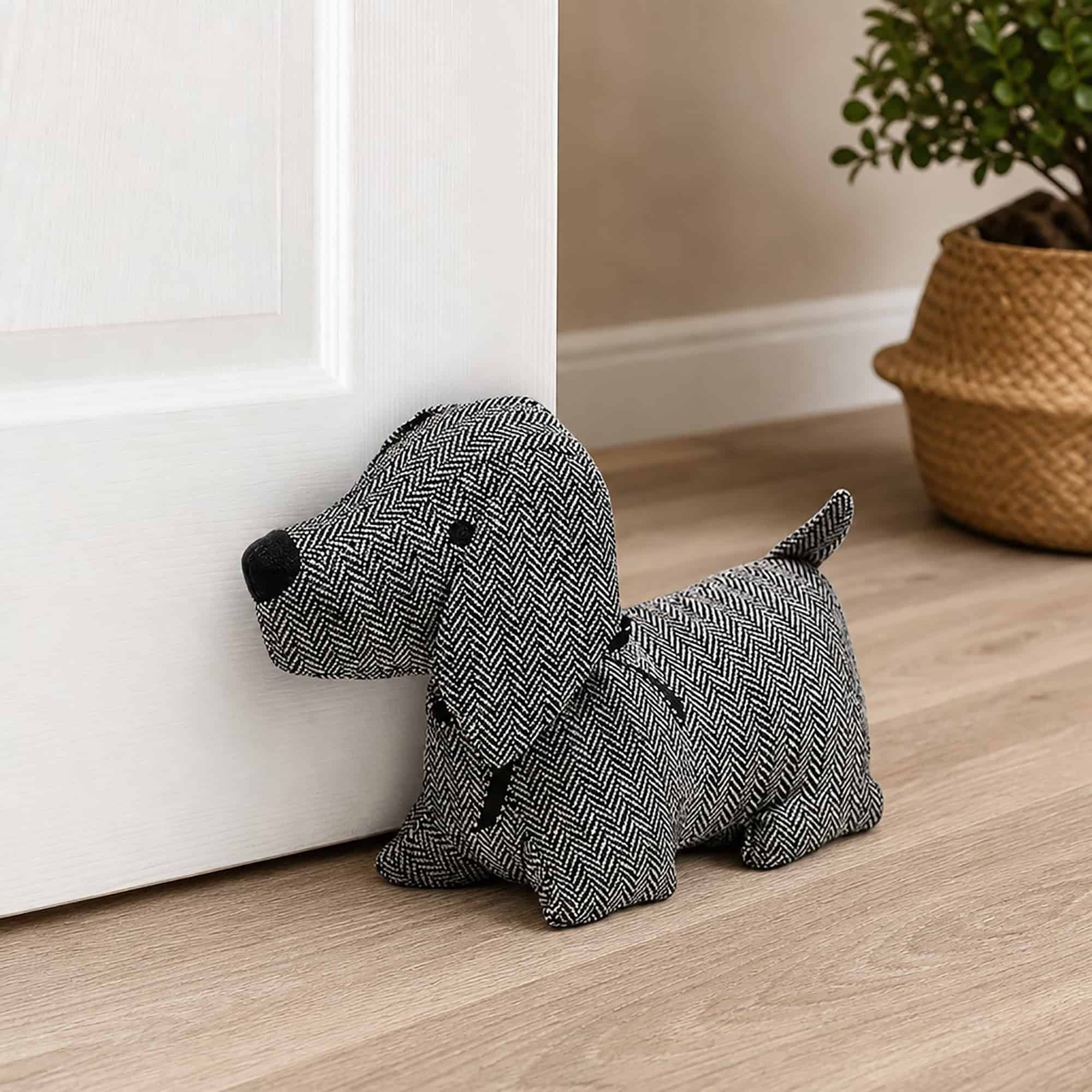 Charcoal dog door stopper propping open a white paneled door, hardwood floor, woven basket with a plant in the background.