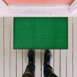 Top view of green synthetic grass door mat placed on wooden floor