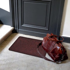 Maroon entry mat placed at an indoor doorway with leather bag