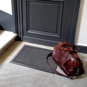 Gray striped entry door mat placed in front of dark door with travel bag