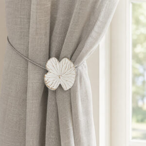 Lifestyle grège: White water lily magnetic tieback holding a light gray sheer linen curtain by a sunlit window