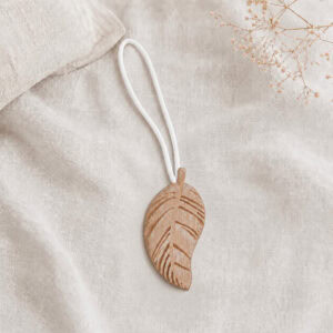 Single natural wood leaf magnetic curtain tieback resting on linen fabric