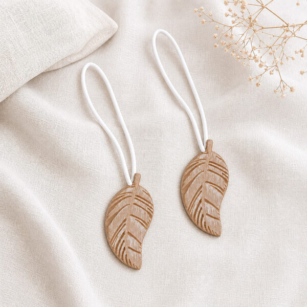 Set of 2 natural wood leaf magnetic curtain tiebacks resting together on linen