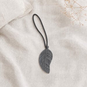 Single gray leaf magnetic curtain tieback resting on natural linen fabric