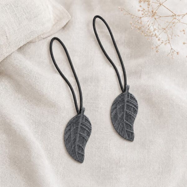 Set of 2 gray leaf magnetic curtain tiebacks resting together on natural linen