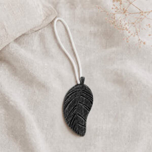 Single black leaf magnetic curtain tieback resting on natural linen fabric
