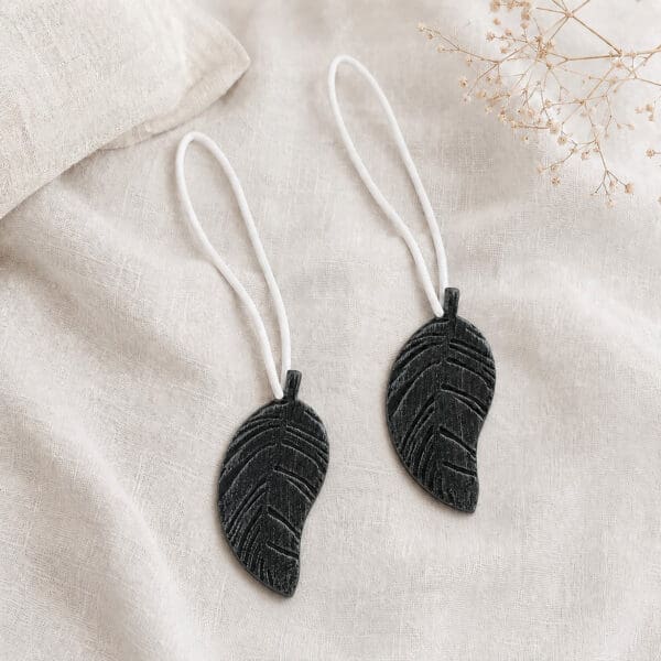 Set of 2 black leaf magnetic curtain tiebacks resting together on natural linen