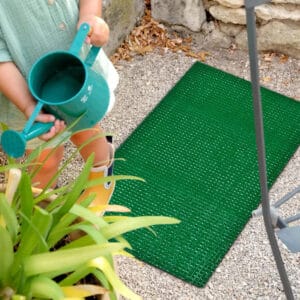 Outdoor green grass doormat placed on stone patio near entry