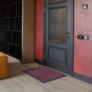 Red burgundy indoor outdoor doormat placed by sliding door on wood floor