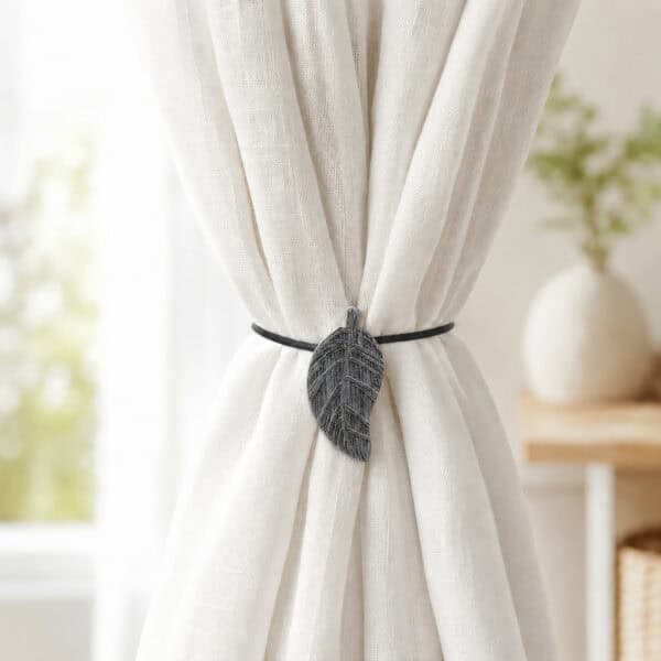 Gray leaf magnetic tieback holding back a light linen curtain by a bright window