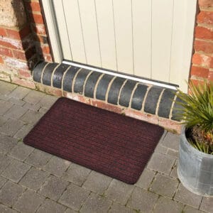 Maroon outdoor doormat in front of an exterior door on stone pavers
