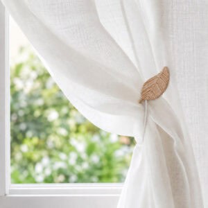 Natural wood leaf magnetic tieback holding a sheer voile curtain in a sunlit room