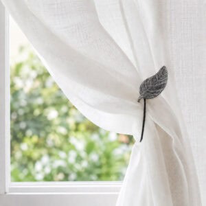 Gray leaf magnetic tieback holding a sheer voile curtain in a sunlit room