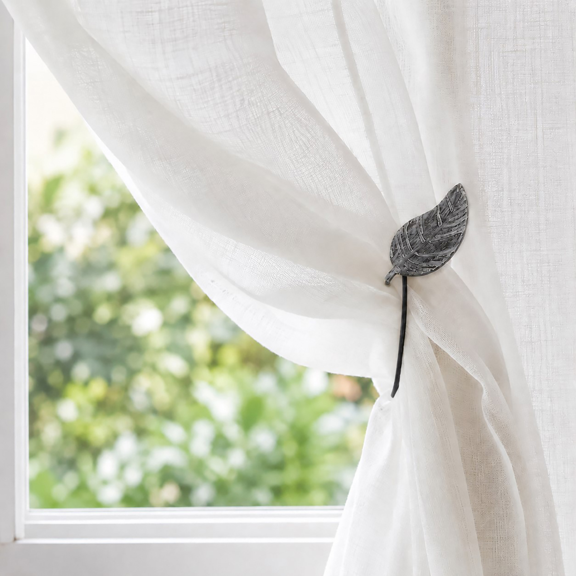 Gray leaf magnetic tieback holding a sheer voile curtain in a sunlit room