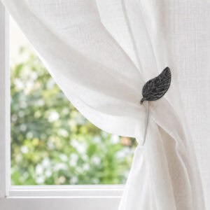 Black leaf magnetic tieback holding a sheer voile curtain in a sunlit room
