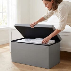 "Woman opening gray faux leather storage ottoman bench lid to place folded linens inside"