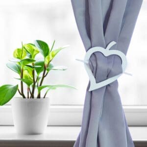 "White wood heart tieback on gray curtain beside green houseplant"