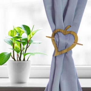 "Natural wood heart tieback on lavender curtain beside green houseplant"