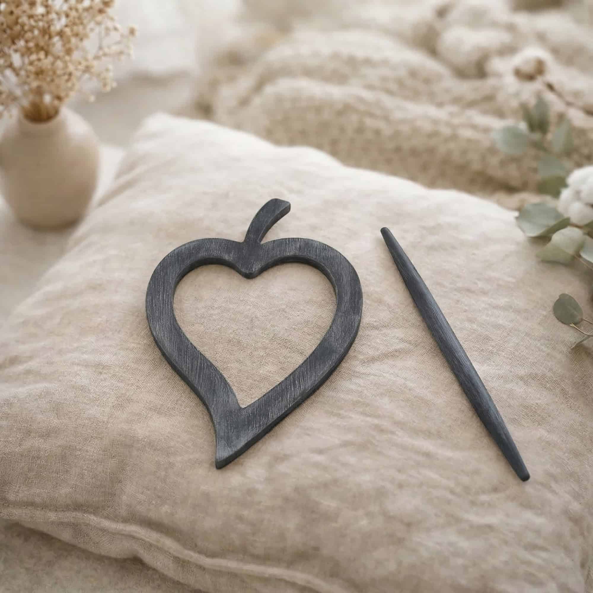 "Dark gray washed wood heart frame and pin displayed on linen cushion"