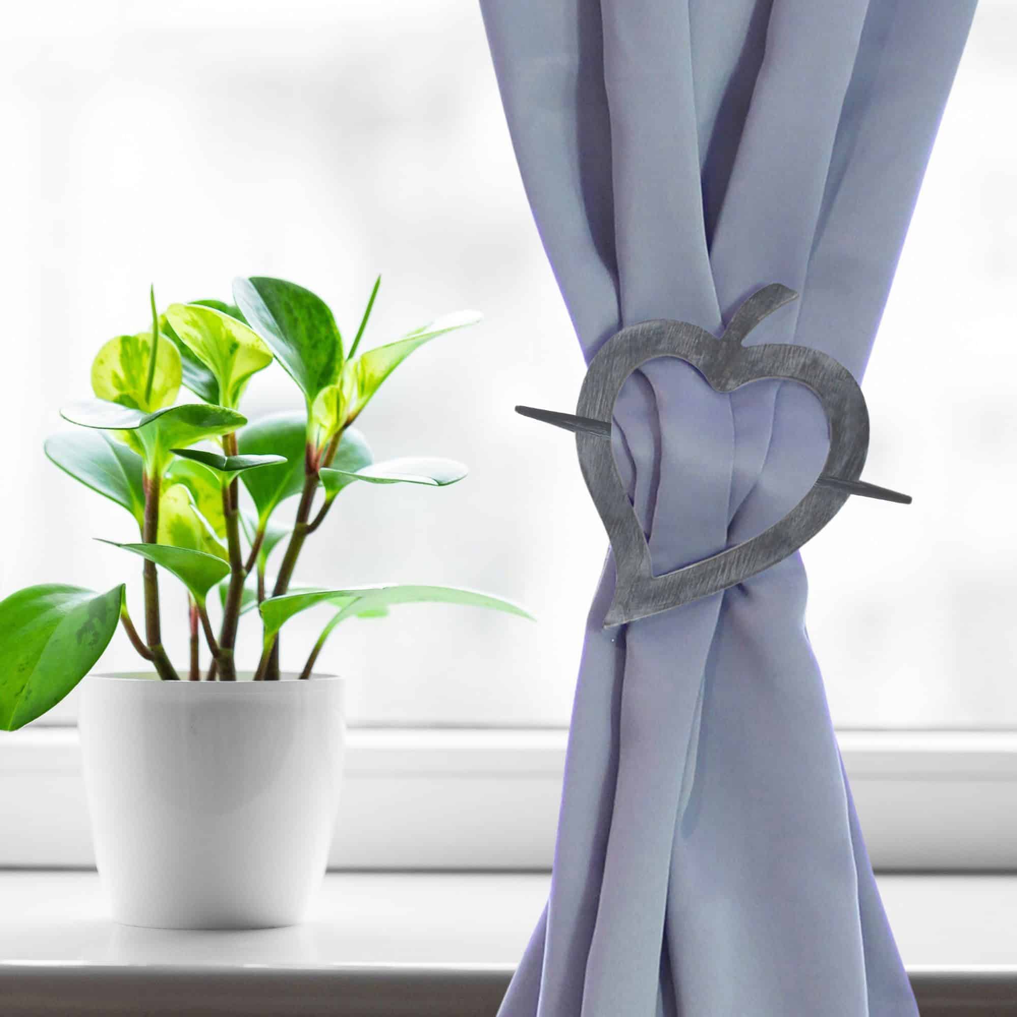 "Gray wood heart tieback on lavender curtain beside green houseplant"