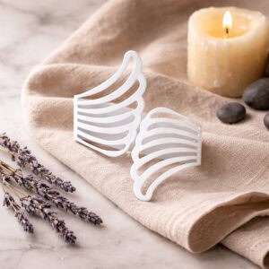 "Pair of white metal wings tiebacks displayed on linen fabric with lavender and candle"