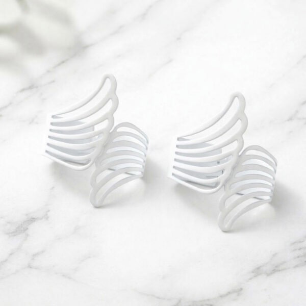"Two white metal angel wings curtain tiebacks displayed on a marble surface"