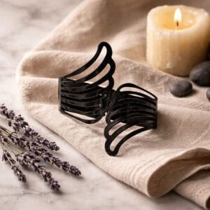 "Pair of black metal wings tiebacks displayed on linen fabric with lavender and candle"