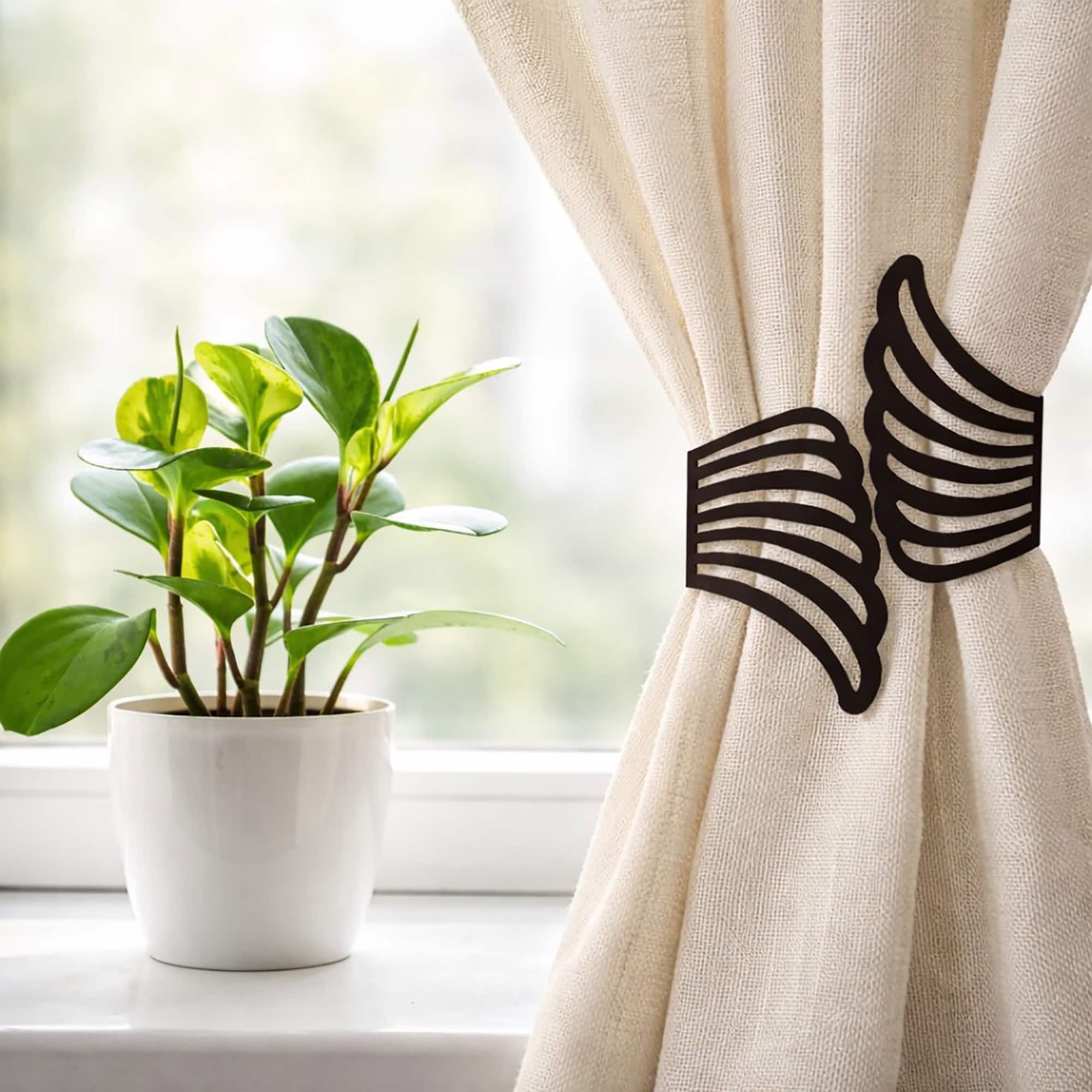 "Black angel wings tieback on cream curtain beside a potted plant on a windowsill"
