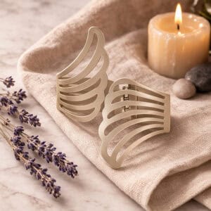 "Pair of gold metal wings tiebacks displayed on linen fabric with lavender and candle"