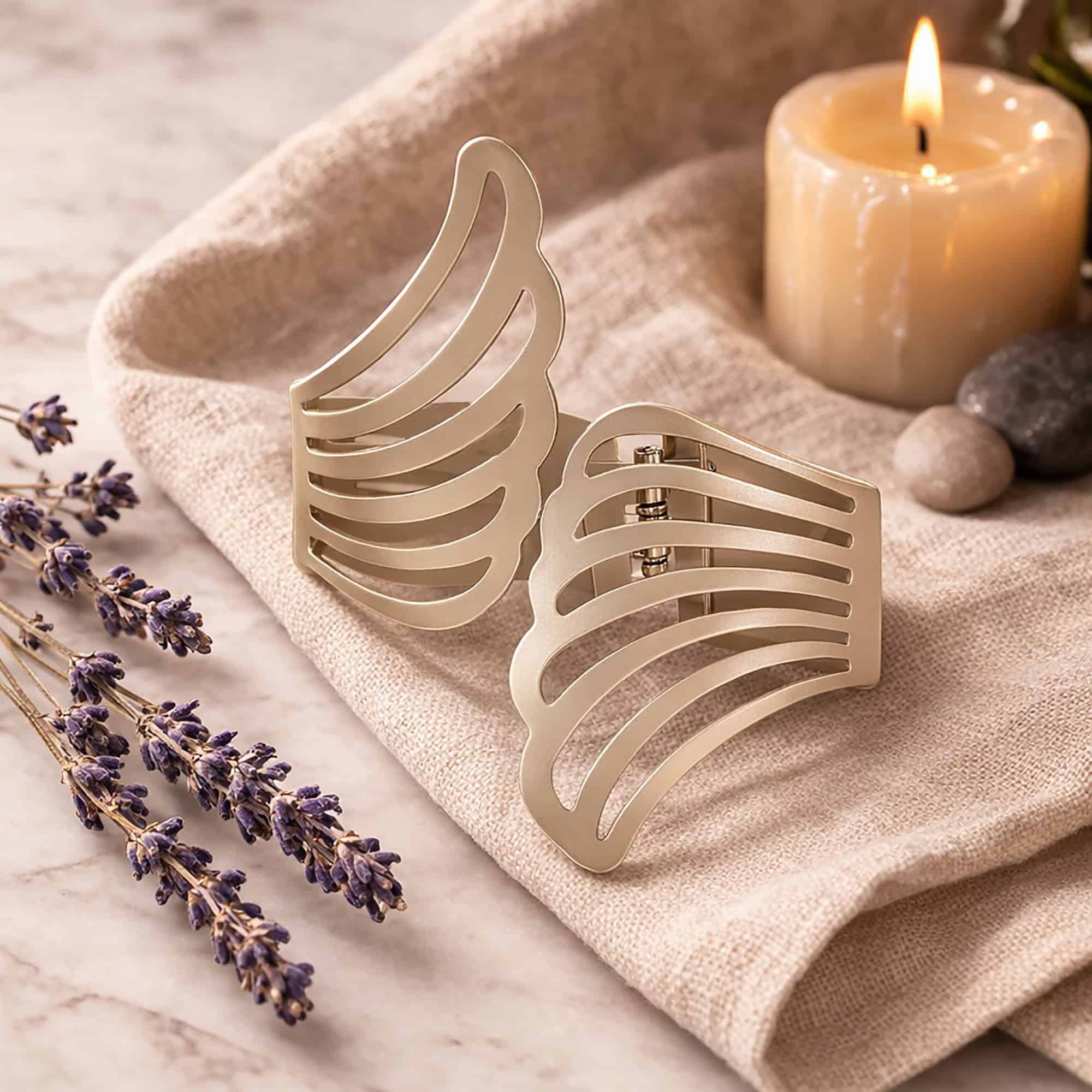 "Pair of gold metal wings tiebacks displayed on linen fabric with lavender and candle"