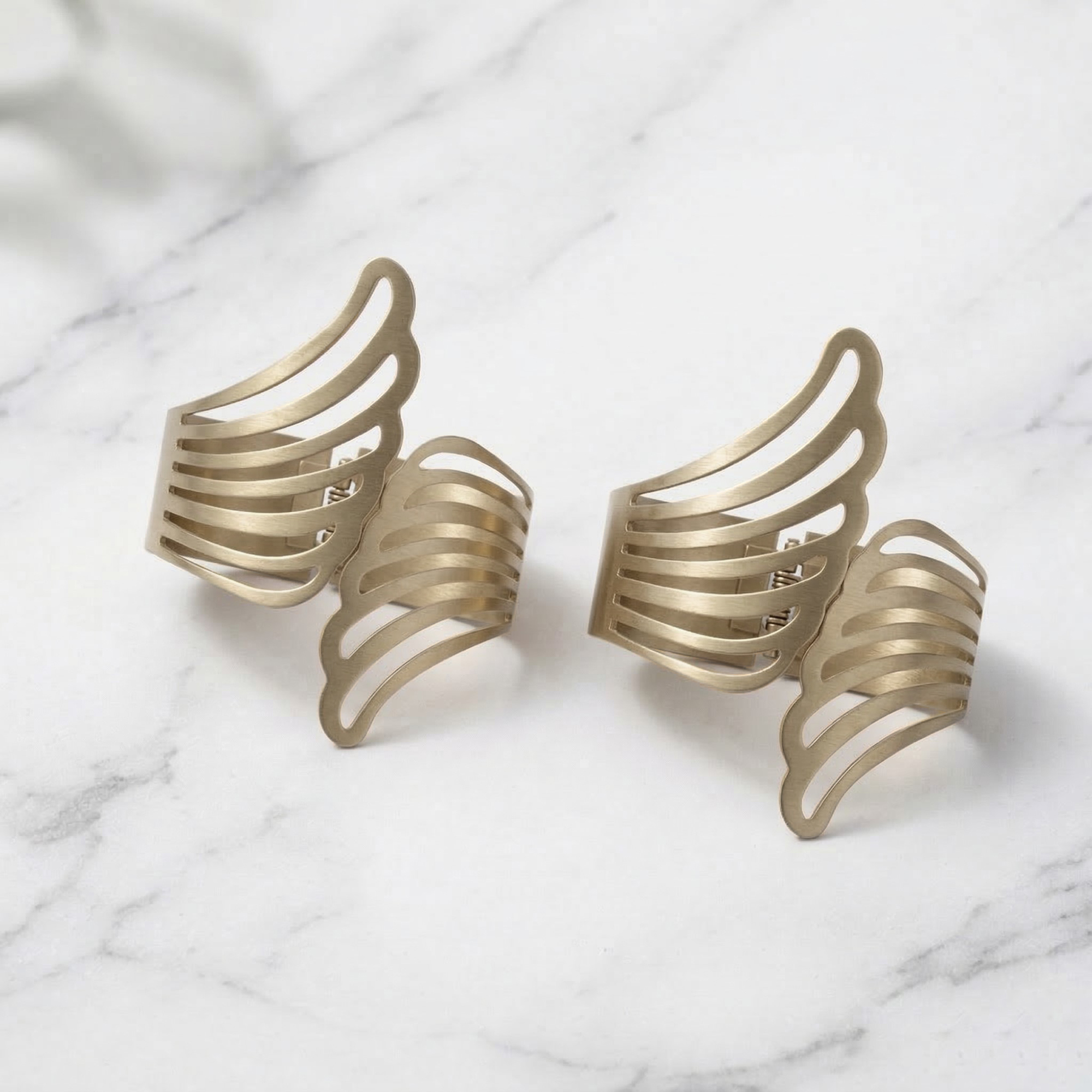 "Two gold metal angel wings curtain tiebacks displayed on a marble surface"