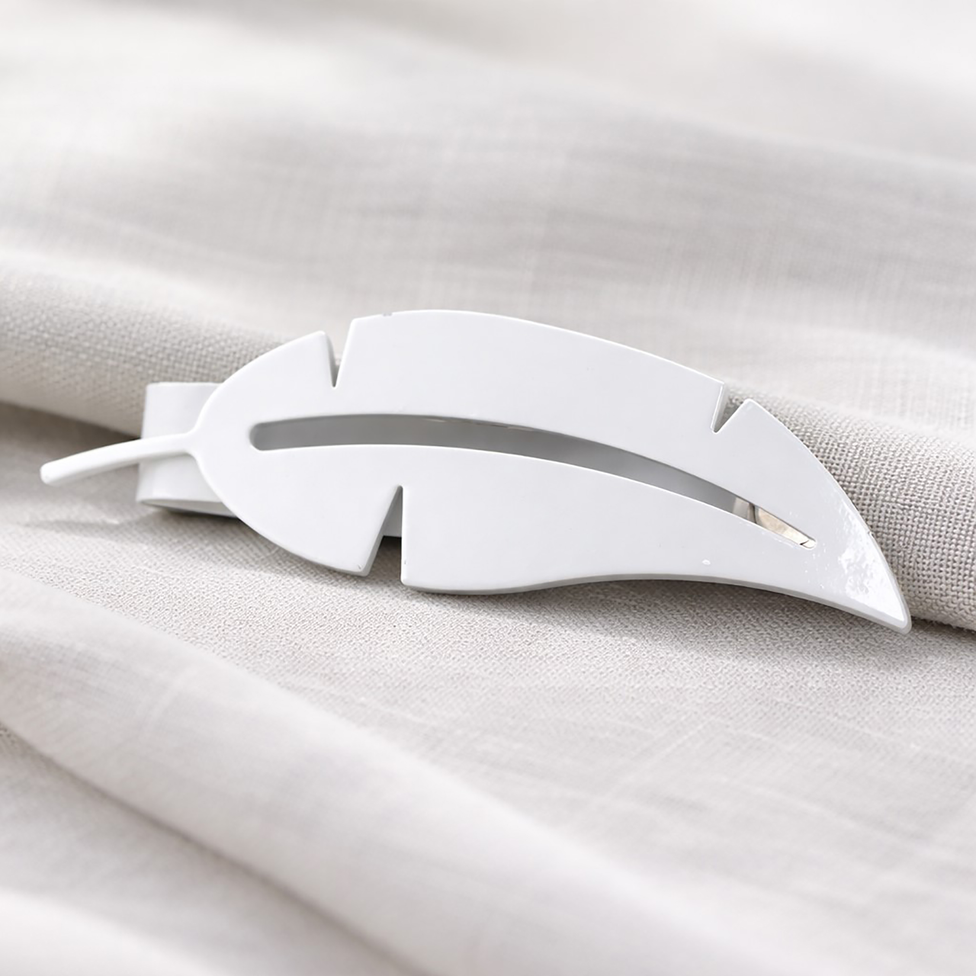 "Close-up of white shiny metal feather tieback on fabric"