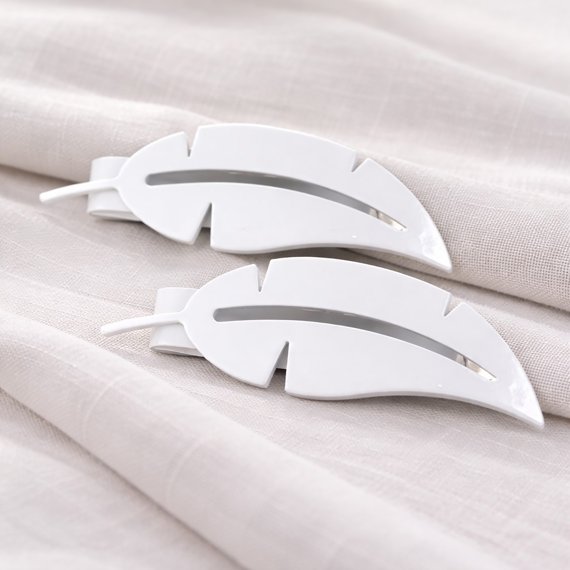"Close-up of white shiny metal feather tiebacks on fabric"