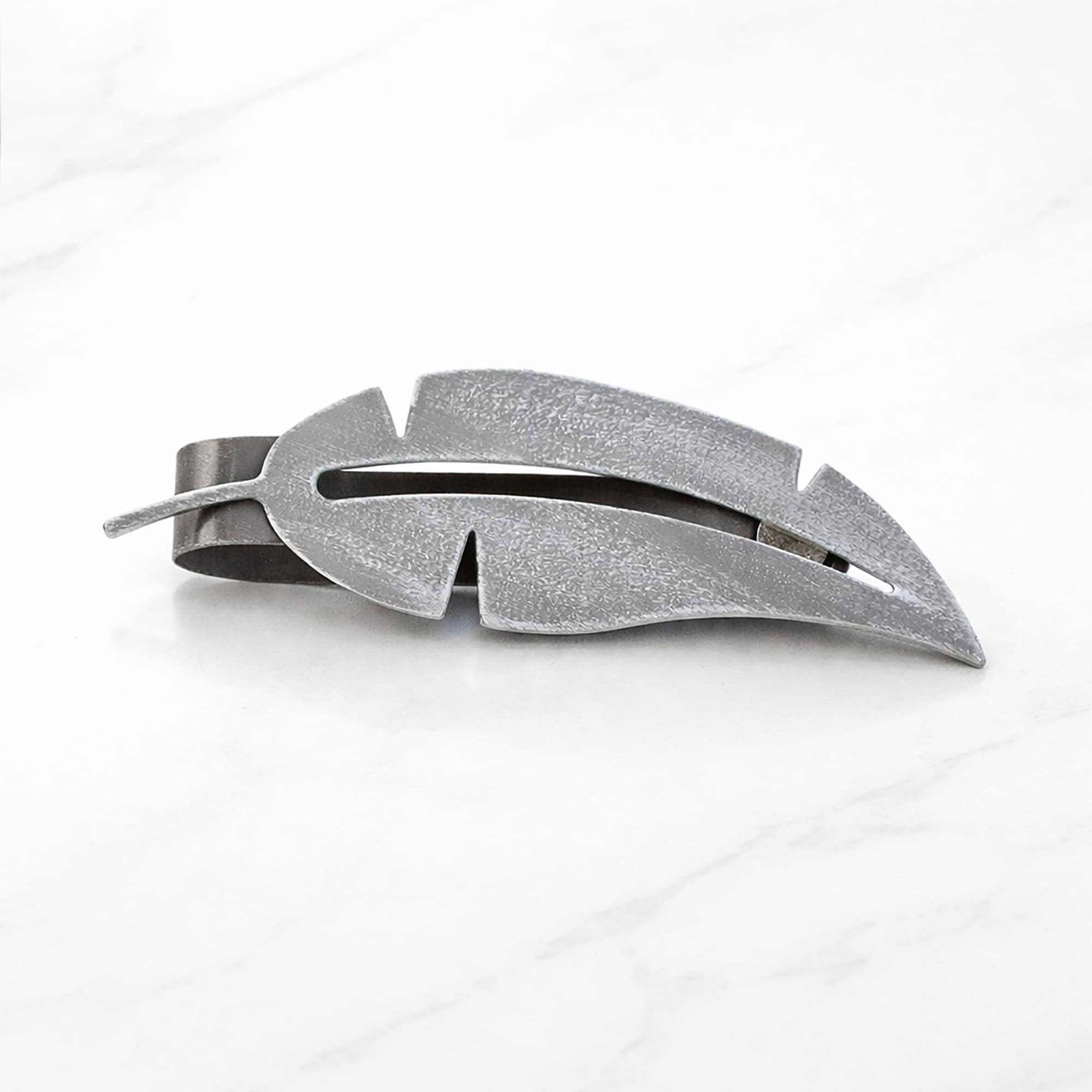 "Grey textured metal feather tieback on marble surface"