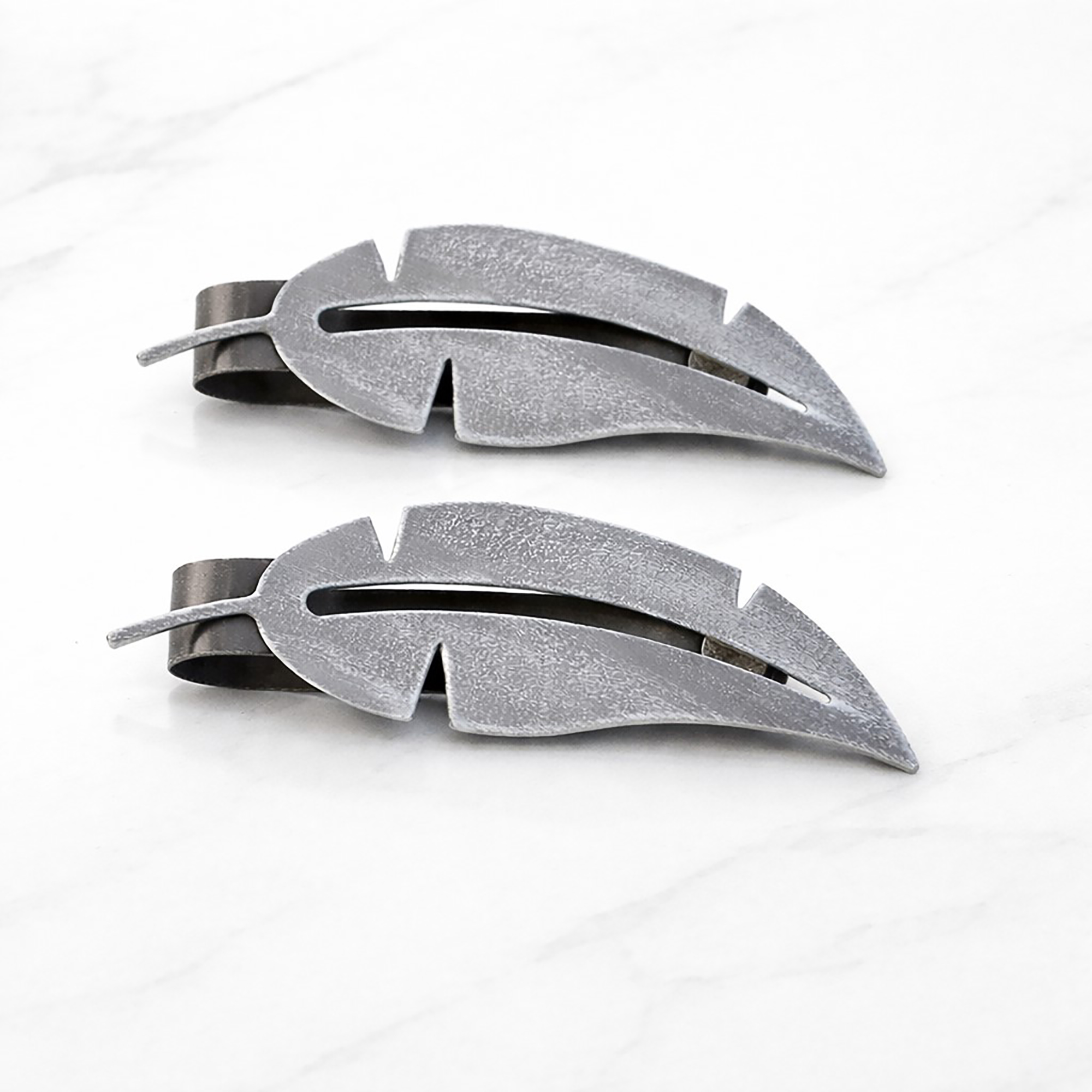 "Grey textured metal feather tiebacks on marble surface"