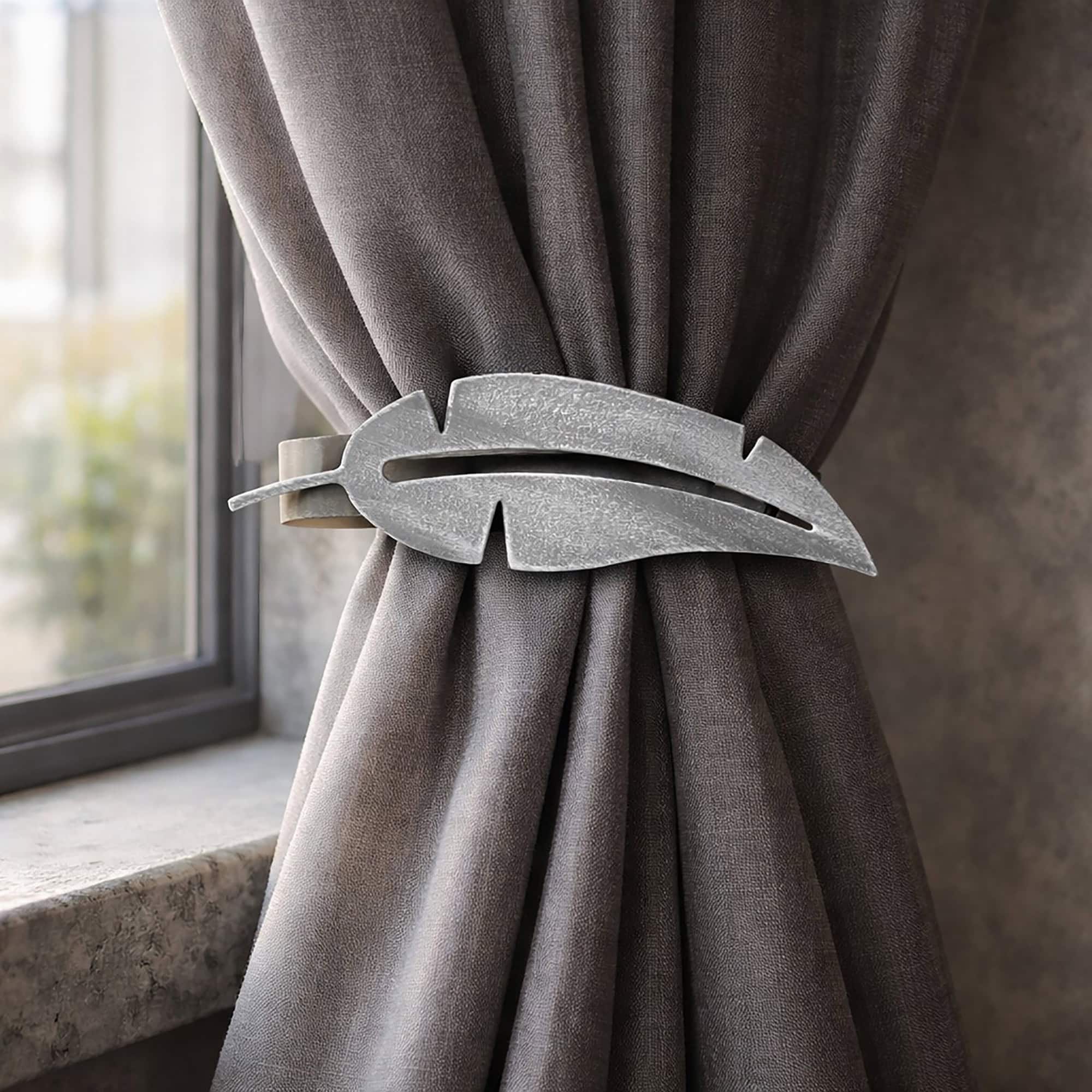 "Grey metal feather tieback holding grey curtain by window"