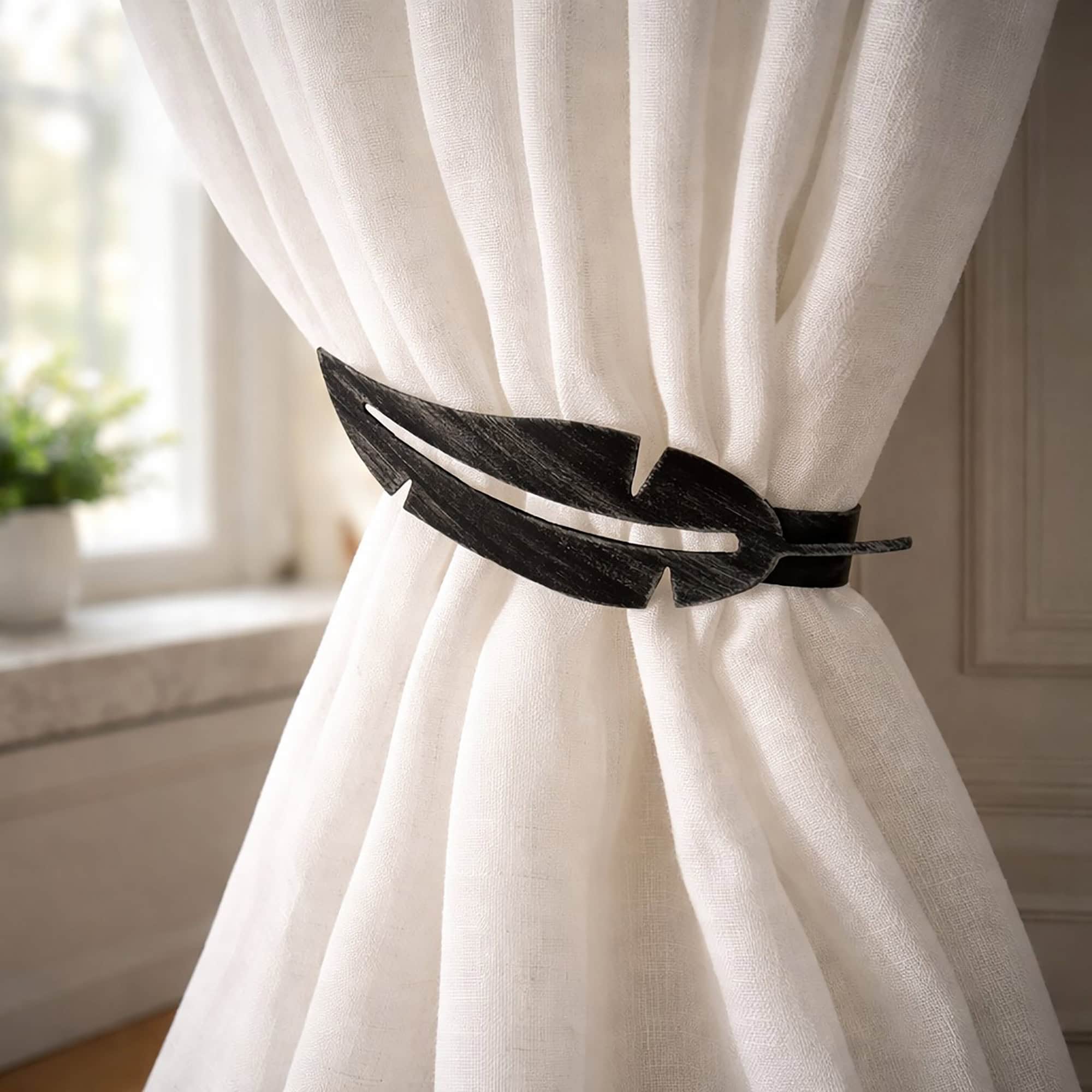 "Black feather metal tieback holding white curtain against wall"