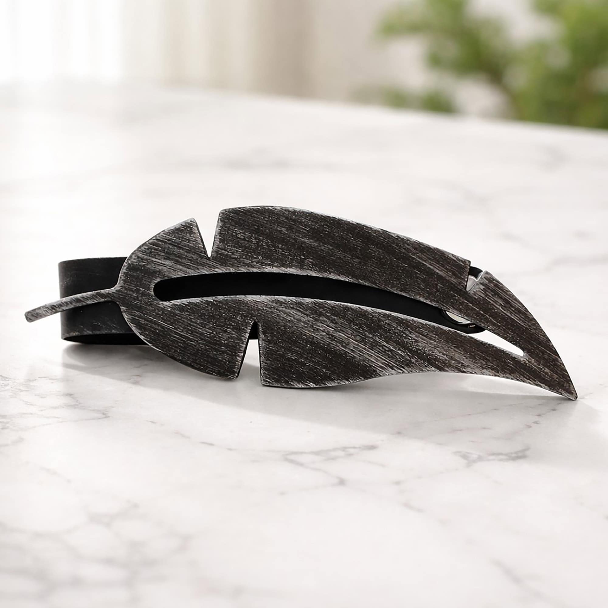 "Black brushed metal feather tieback on marble surface"