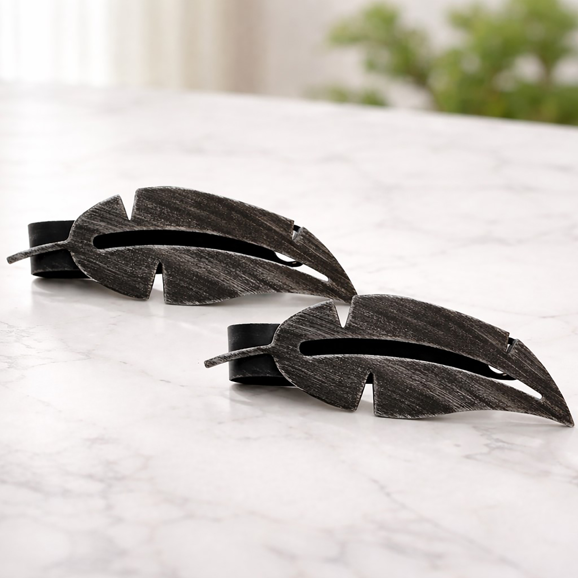 "Black brushed metal feather tiebacks on marble surface"