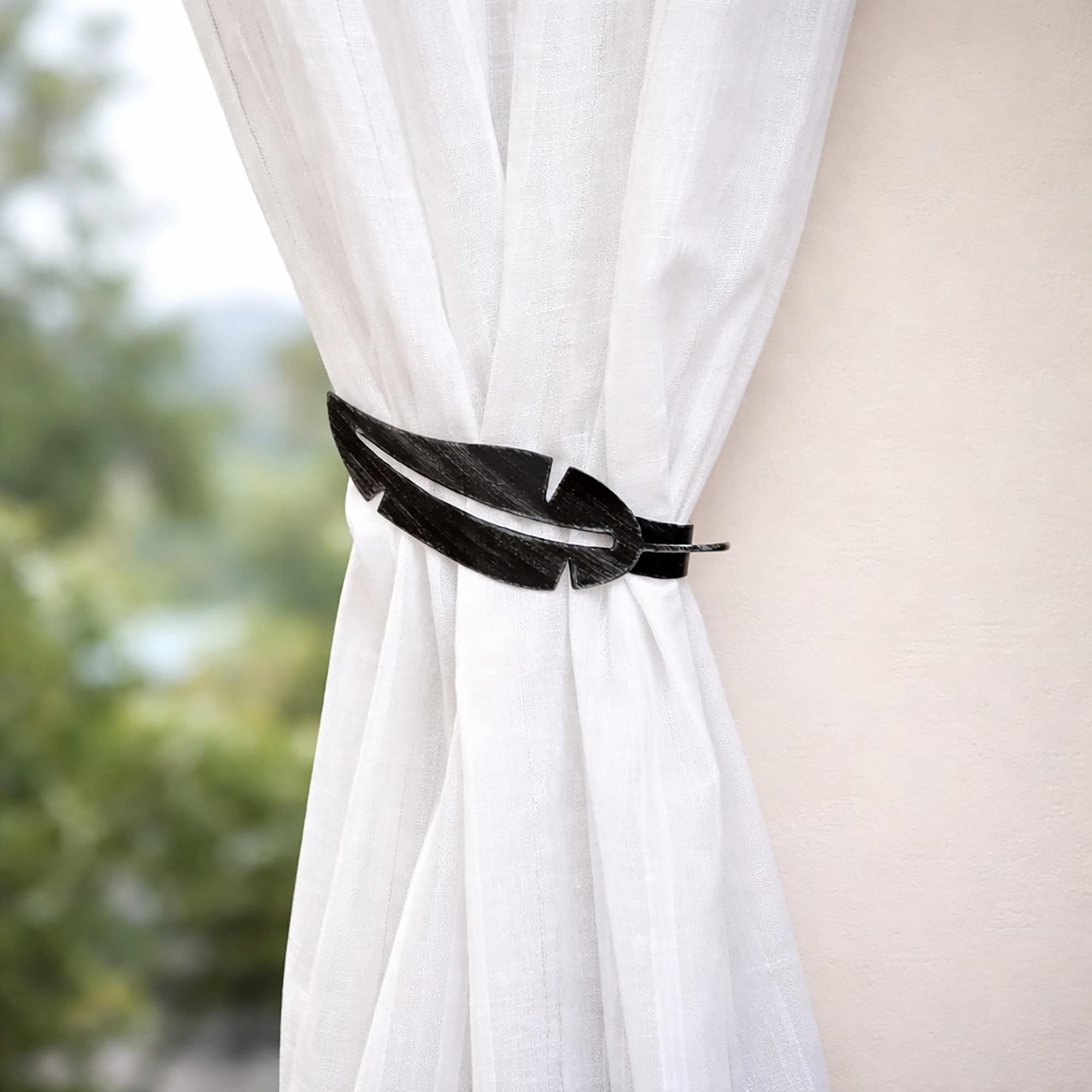 "Black feather tieback on sheer white curtain against neutral wall"
