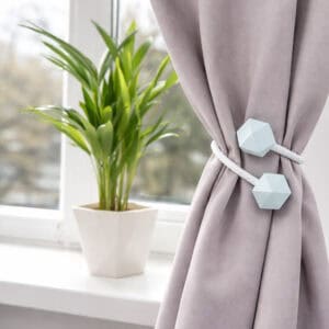 White geometric tieback bundling a mauve curtain near a sunlit window with indoor plant